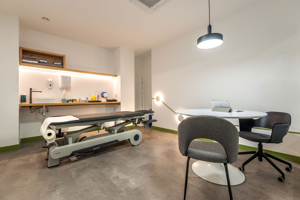 Habitación con una camilla de fisioterapia, una mesa y sillas